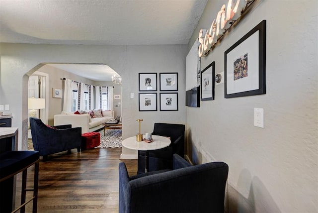living area featuring a textured ceiling, a textured wall, arched walkways, and wood finished floors