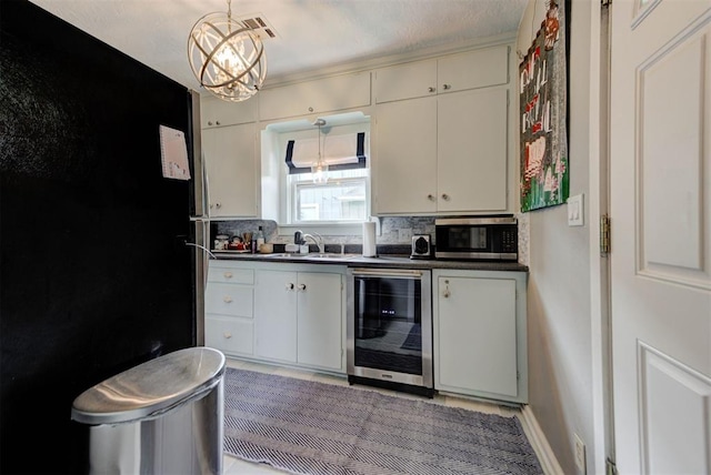 kitchen with a sink, stainless steel microwave, wine cooler, a chandelier, and dark countertops