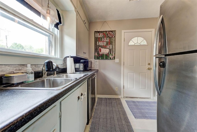 kitchen with freestanding refrigerator, dishwashing machine, baseboards, and a sink