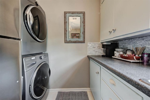 clothes washing area featuring baseboards, stacked washer and dryer, and cabinet space