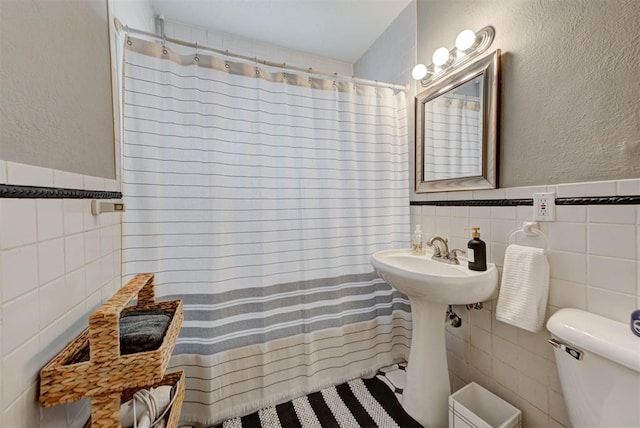 full bath featuring tile walls, toilet, curtained shower, a textured wall, and wainscoting