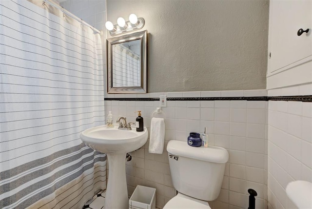 bathroom with a shower with curtain, tile walls, toilet, wainscoting, and a textured wall