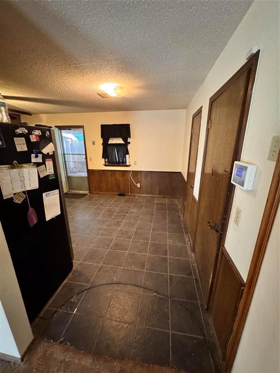 hallway featuring wooden walls, a textured ceiling, and wainscoting