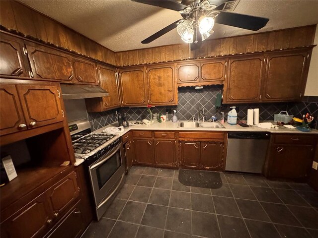 kitchen with decorative backsplash, a textured ceiling, under cabinet range hood, a sink, and stainless steel appliances