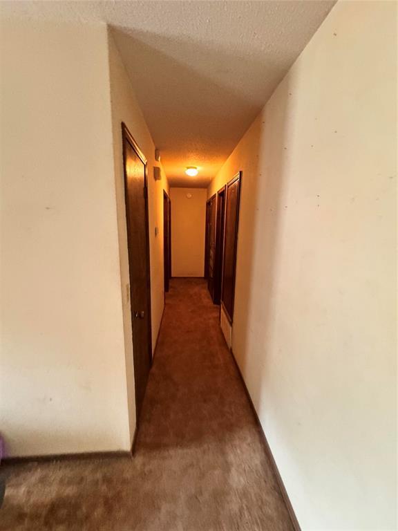 hall with a textured ceiling and light colored carpet