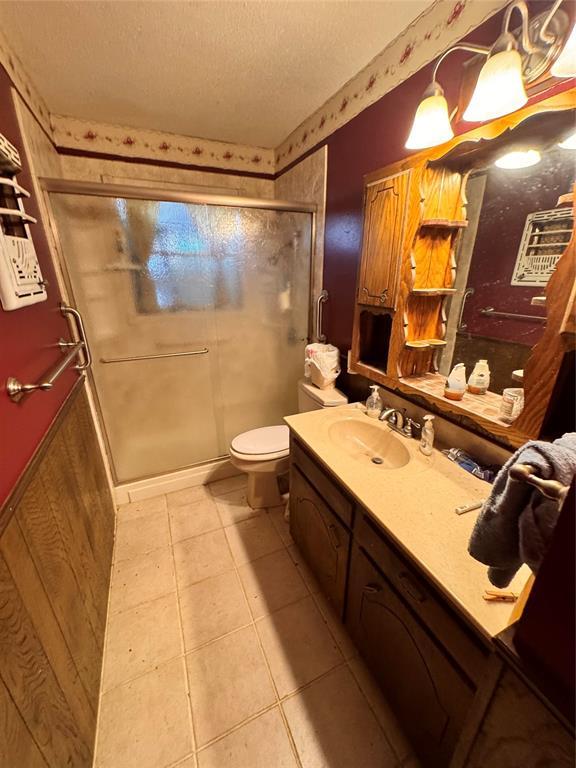 full bathroom featuring a textured ceiling, a shower stall, vanity, tile patterned floors, and toilet