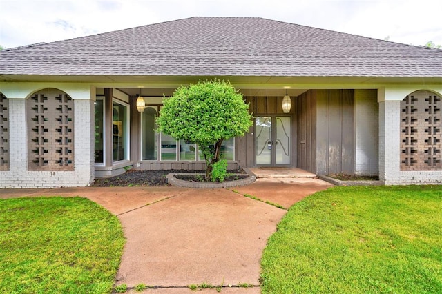 doorway to property with a yard, brick siding, and a shingled roof