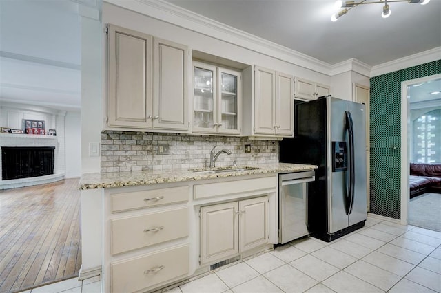 kitchen with appliances with stainless steel finishes, light stone counters, a sink, ornamental molding, and glass insert cabinets