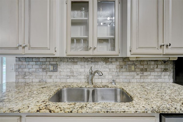kitchen featuring backsplash, light stone countertops, glass insert cabinets, and a sink