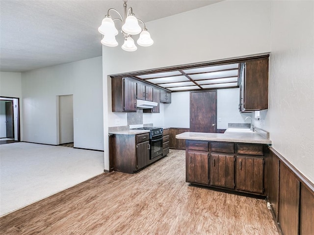 1357 W Cedarbrook Ln, Moore, OK 73170 - kitchen with light countertops, dark brown cabinetry, under cabinet range hood, a notable chandelier, and black gas range