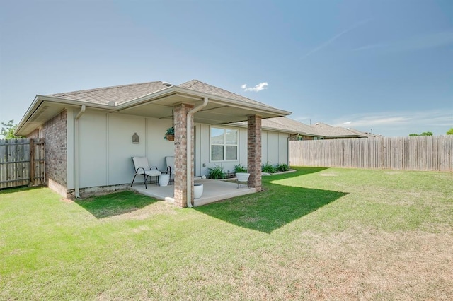 rear view of property featuring a yard, a shingled roof, a fenced backyard, and a patio area