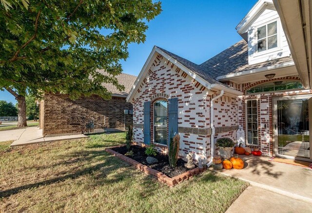 view of home's exterior with roof with shingles, a yard, and brick siding