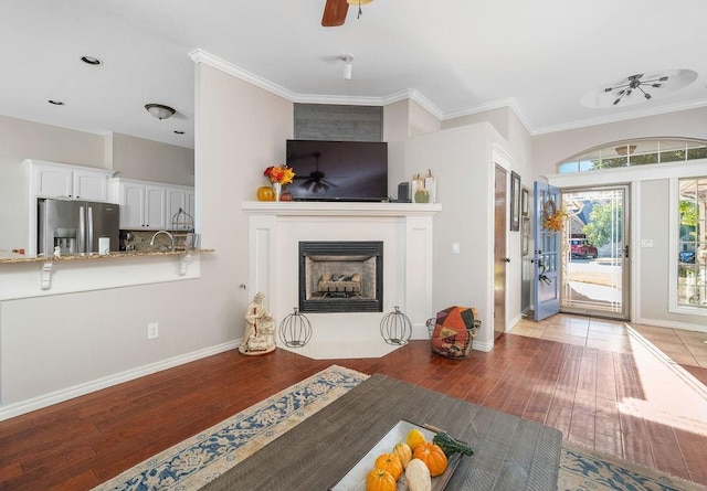 living room featuring ceiling fan, a fireplace with flush hearth, crown molding, light wood-type flooring, and baseboards