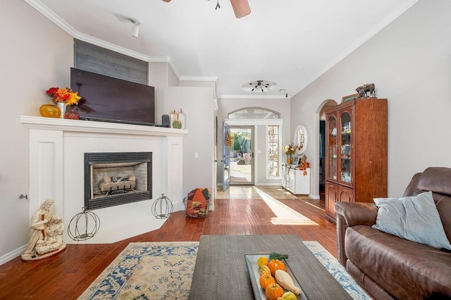 living area with crown molding, a fireplace with flush hearth, ceiling fan, and wood finished floors