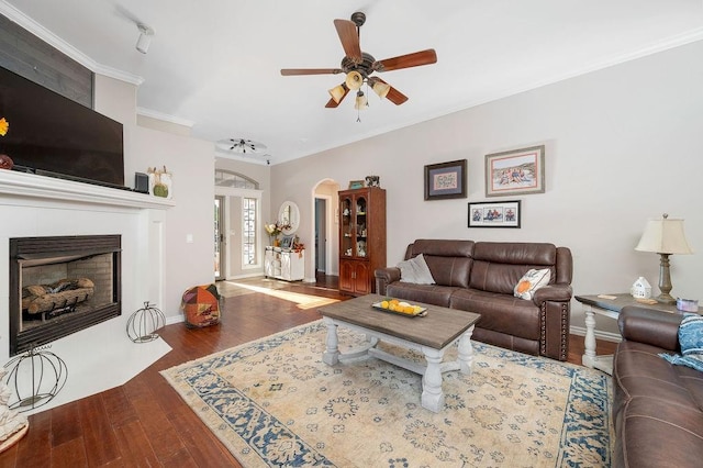 living room with a ceiling fan, crown molding, arched walkways, a fireplace with flush hearth, and wood finished floors