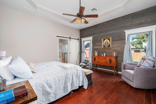 bedroom with visible vents, wood walls, wood-type flooring, an accent wall, and a barn door