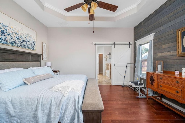 bedroom with a barn door, wood walls, wood finished floors, a tray ceiling, and visible vents