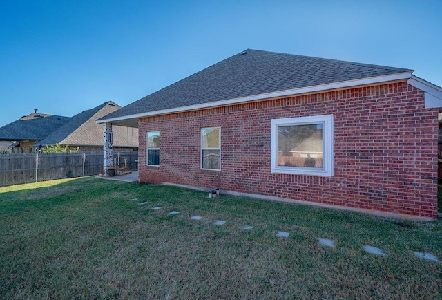 rear view of property with a yard, brick siding, fence, and roof with shingles