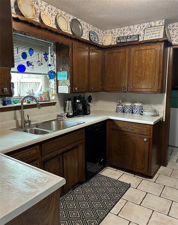 kitchen featuring black dishwasher, a textured ceiling, a sink, and light countertops