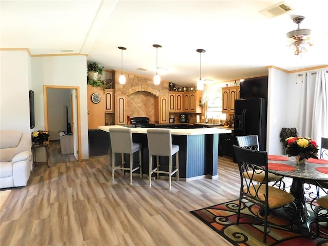 kitchen featuring a kitchen island, brown cabinets, light wood finished floors, visible vents, and black fridge