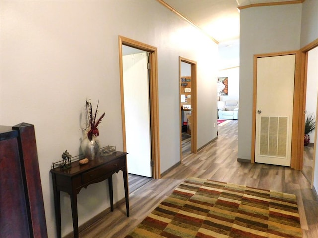 corridor with wood finished floors, visible vents, and crown molding