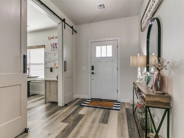 foyer with visible vents, a barn door, wood finished floors, and a wealth of natural light
