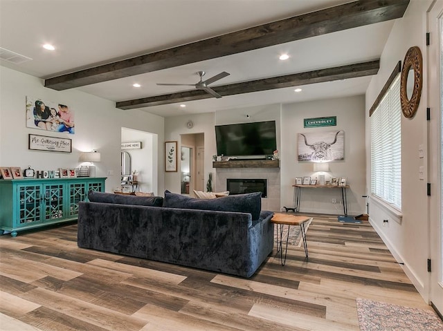 living room with visible vents, a ceiling fan, a glass covered fireplace, and wood finished floors