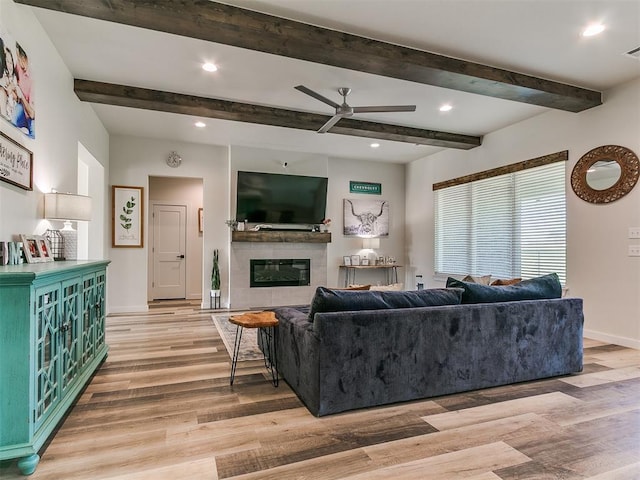 living area with baseboards, light wood finished floors, a glass covered fireplace, and ceiling fan