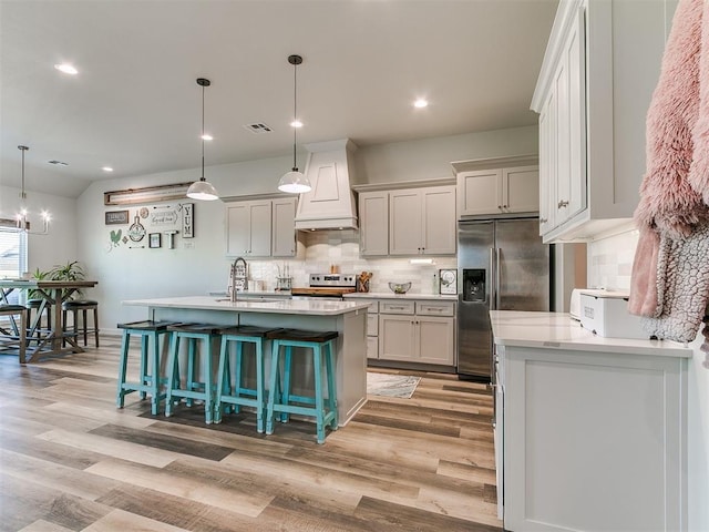 kitchen with light wood finished floors, custom exhaust hood, tasteful backsplash, and stainless steel appliances