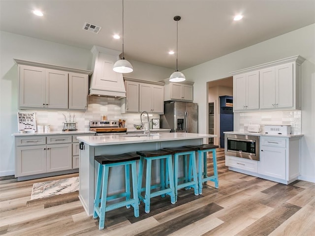 kitchen with visible vents, decorative backsplash, premium range hood, a sink, and stainless steel appliances