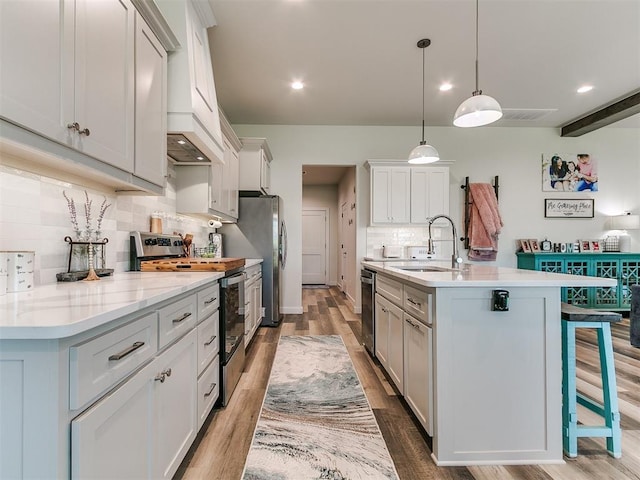 kitchen with a kitchen island with sink, backsplash, appliances with stainless steel finishes, a sink, and light countertops