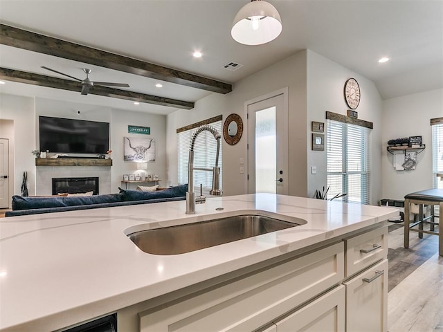 kitchen with open floor plan, white cabinets, light stone counters, a sink, and light wood-style flooring