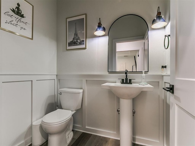 half bath with a wainscoted wall, a decorative wall, toilet, and wood finished floors