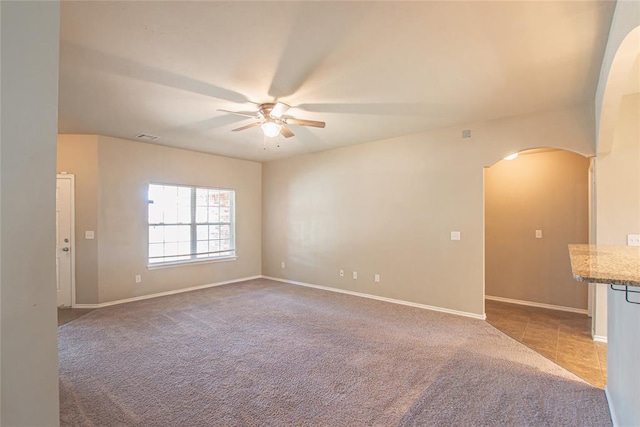 carpeted empty room featuring arched walkways, ceiling fan, visible vents, and baseboards