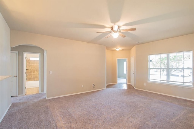 carpeted empty room featuring arched walkways, baseboards, and a ceiling fan
