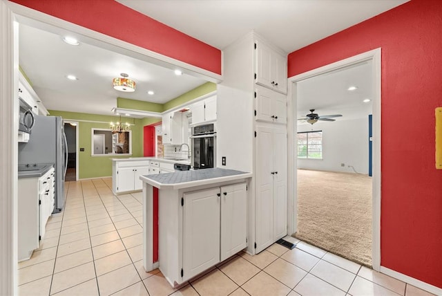 kitchen with appliances with stainless steel finishes, a sink, a peninsula, light carpet, and white cabinetry