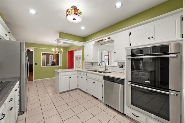 kitchen featuring white cabinets, a sink, light tile patterned floors, a notable chandelier, and stainless steel appliances