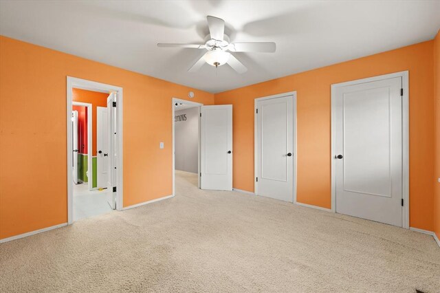 unfurnished bedroom featuring carpet floors, a ceiling fan, baseboards, and two closets