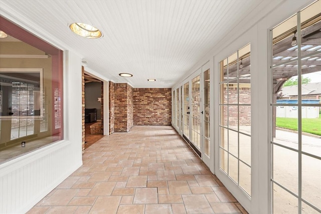 unfurnished sunroom featuring brick wall, stone finish flooring, and french doors