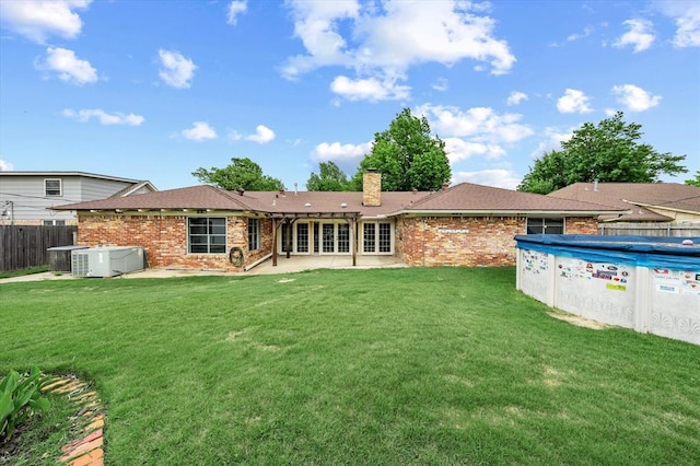 rear view of house featuring a yard, brick siding, fence, and a patio