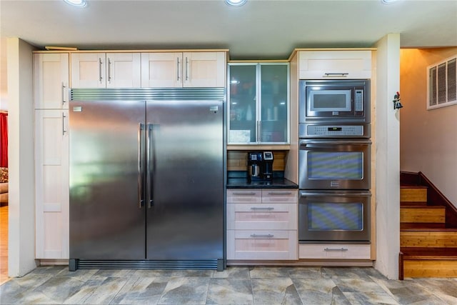 kitchen featuring dark countertops, built in appliances, recessed lighting, visible vents, and glass insert cabinets