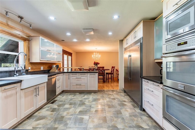 kitchen with built in appliances, a peninsula, dark countertops, recessed lighting, and a sink