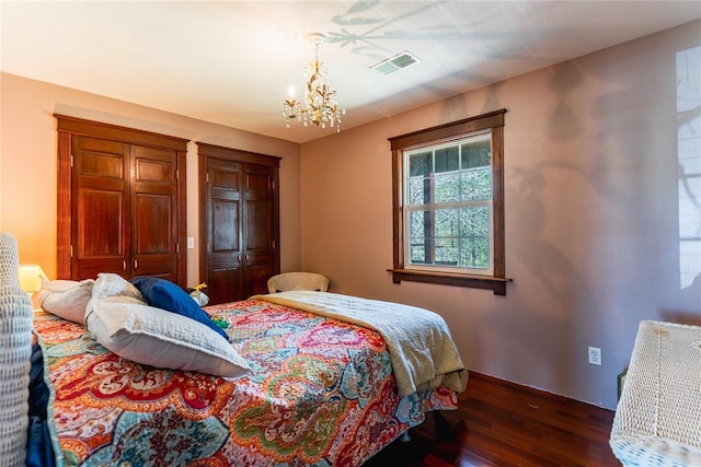 bedroom with multiple closets, a chandelier, baseboards, dark wood-type flooring, and visible vents