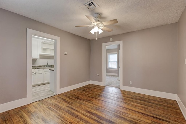 spare room with a sink, ceiling fan, wood finished floors, and visible vents
