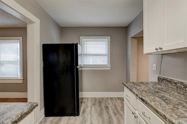 kitchen featuring white cabinets, light stone countertops, light wood-style floors, a textured ceiling, and freestanding refrigerator