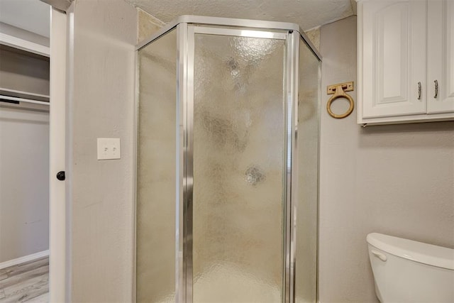 full bathroom featuring a stall shower, toilet, and wood finished floors
