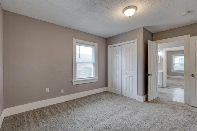 unfurnished bedroom with a textured ceiling, multiple windows, baseboards, and carpet