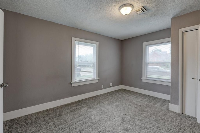carpeted empty room with a healthy amount of sunlight, baseboards, a textured ceiling, and visible vents