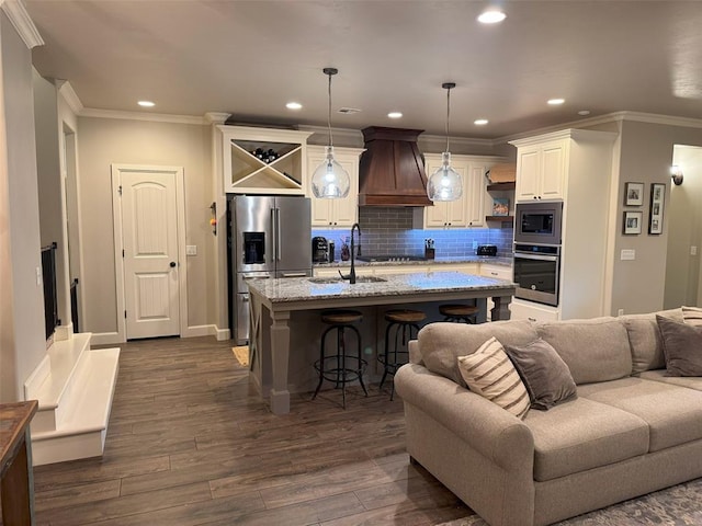 kitchen featuring a sink, stainless steel appliances, premium range hood, open floor plan, and ornamental molding