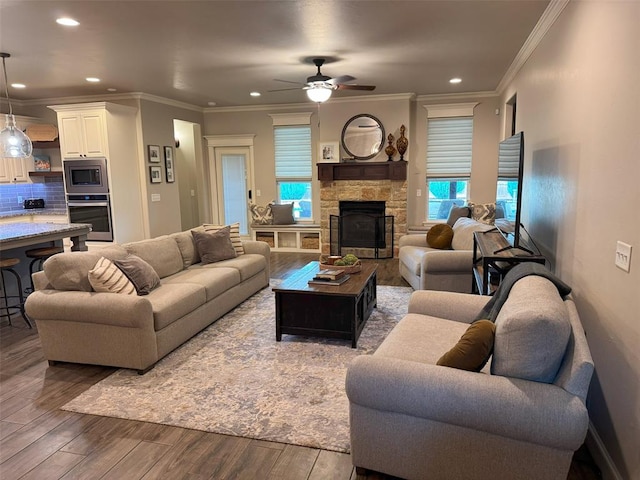 living room with ornamental molding, a ceiling fan, a stone fireplace, and wood finished floors